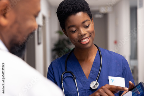 Smiling african american male and female doctor using tablet in hospital corridor