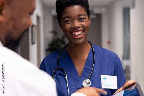 Smiling african american male and female doctor using tablet in hospital corridor