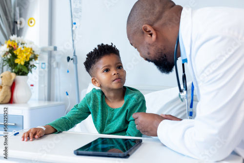 Smiling african american male doctor and boy patient talking in hospital