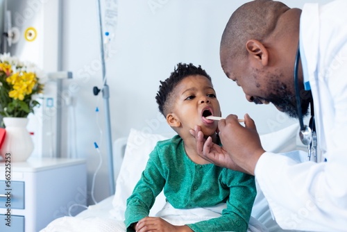 African american male doctor examining mouth of boy patient in hospital