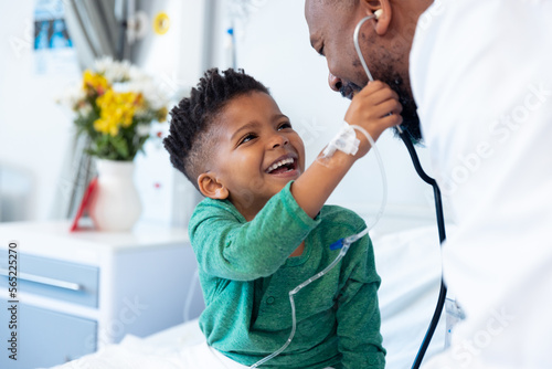 Laughing african american boy patient taking male doctor's stethoscope in hospital