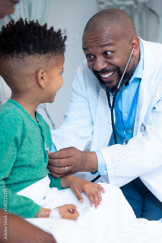 Smiling african american male doctor using stethoscope on boy patient