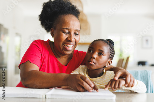 Happy african american grandmother and blind granddaughter reading braille photo