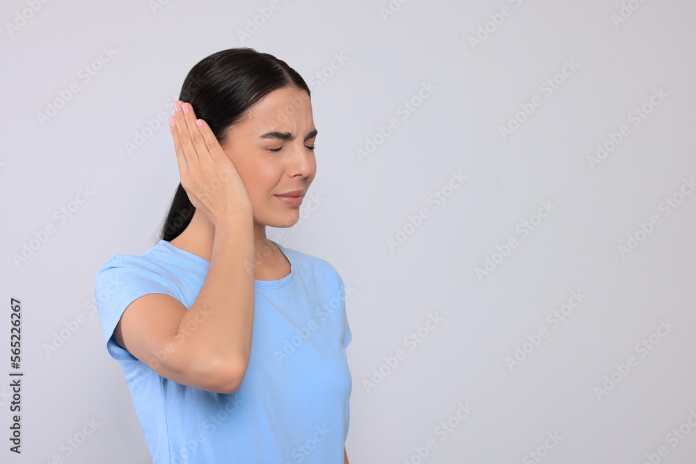 Young woman suffering from ear pain on light grey background. Space for text Young woman suffering from ear pain on light grey background. Space for text