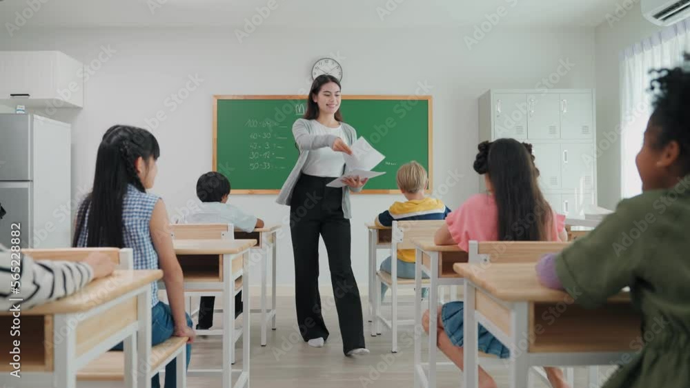 Teacher woman is walking and handing out mathematics exams to elementary school students for final exams Teacher woman is walking and handing out mathematics exams to elementary school students for final exams