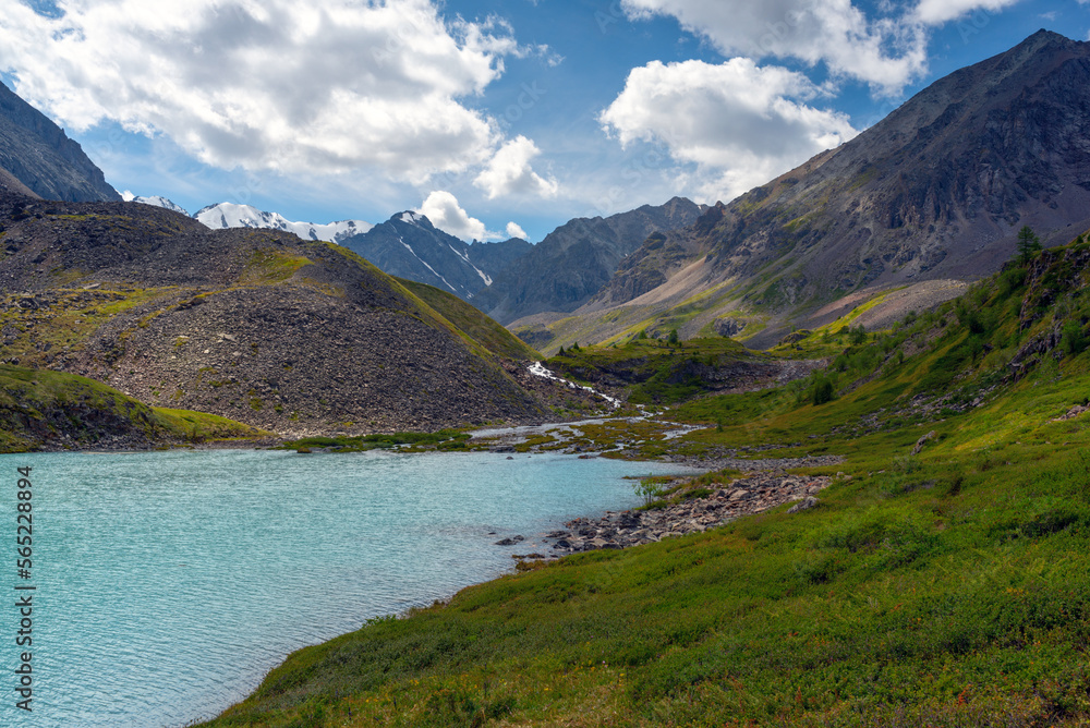 The turquoise mountain lake Karakabak against the background of peaks with snow of glaciers flows down from above in Altai during the day.