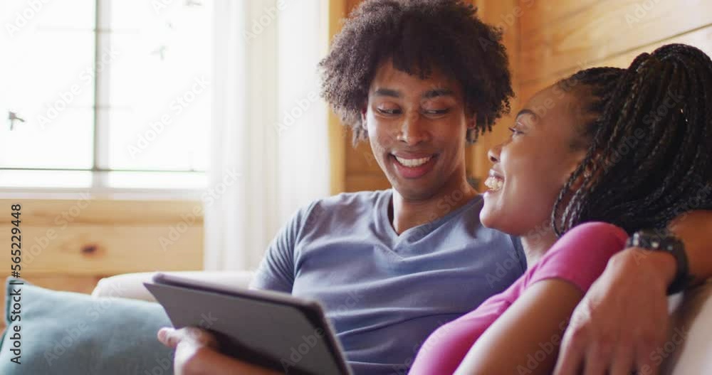 Happy african american couple using tablet, sitting on sofa in log cabin, slow motion Happy african american couple using tablet, sitting on sofa in log cabin, slow motion