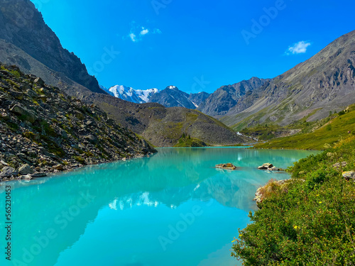 Turquoise mountain lake Karakabak against the background of peaks and stone rocks with a day in Altai in summer among green grass.