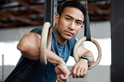Portrait, gymnastic rings and olympics with a man gymnast hanging on equipment for workout in gym. Face, fitness and exercise with a male athlete training in gymnastics for health or power photo