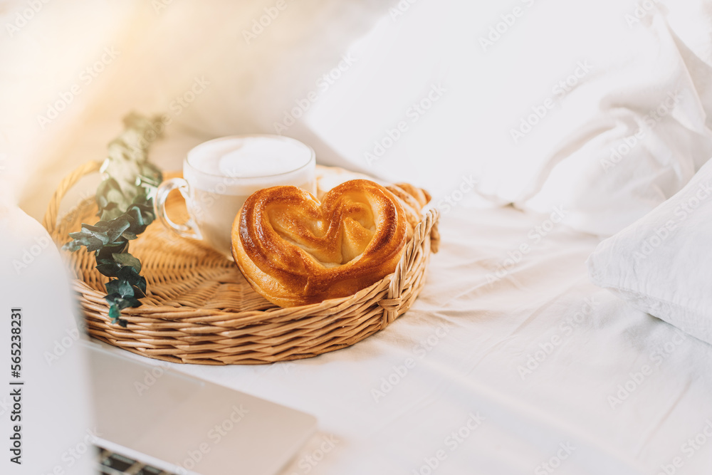 Wicker tray with croissants and coffee on white bed linen with laptop. Wicker tray with croissants and coffee on white bed linen with laptop.