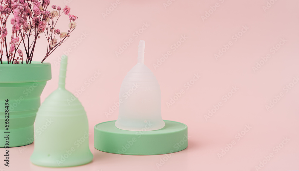 Menstrual cups on green podium next to red dry flowers in power case against pink background. Menstrual cups on green podium next to red dry flowers in power case against pink background.