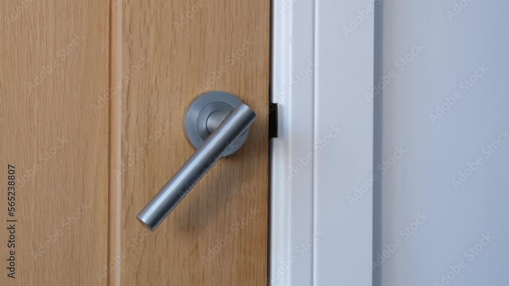 Generic modern interior wooden oak panel door with brushed aluminium silver metal door handle moving up and down. Slowly opening and closing. White grey wall and frame. Close up Generic modern interior wooden oak panel door with brushed aluminium silver metal door handle moving up and down. Slowly opening and closing. White grey wall and frame. Close up