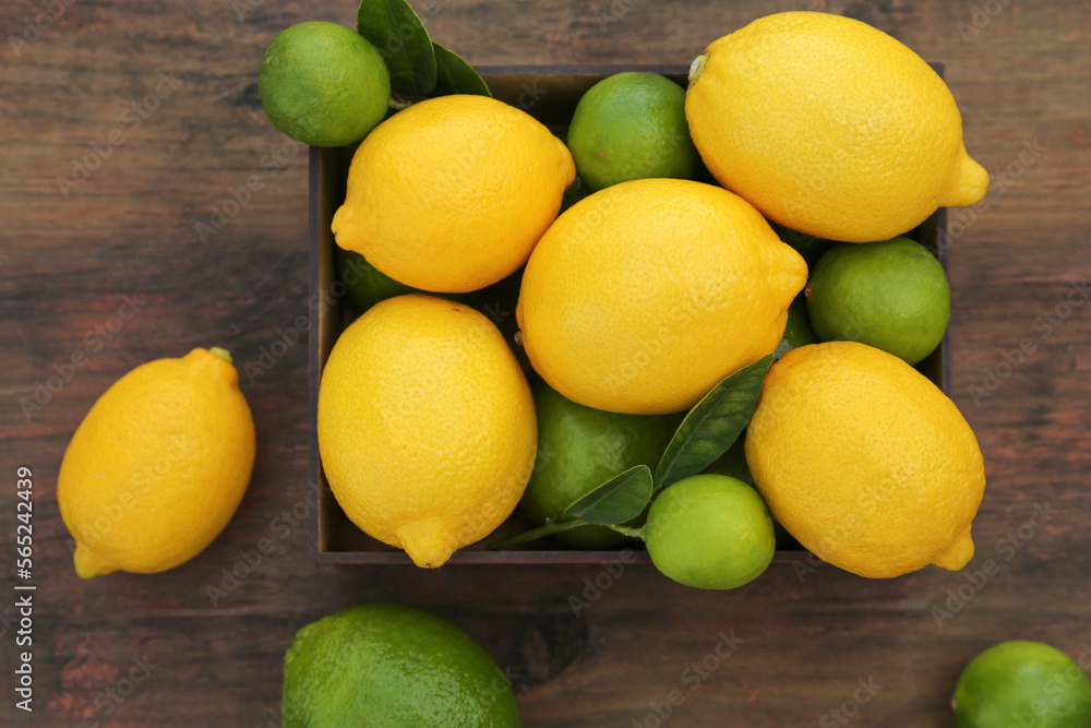 Many fresh lemons and limes with leaves on wooden table, flat lay