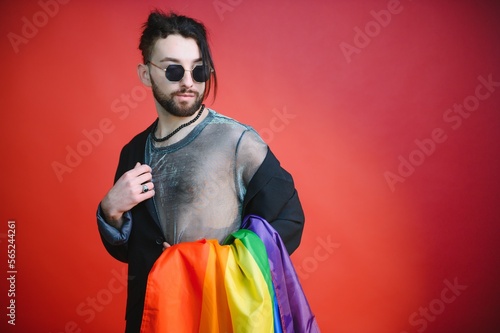 Handsome young man with pride movement LGBT Rainbow flag on shoulder against white background. Man with a gay pride flag. © Serhii