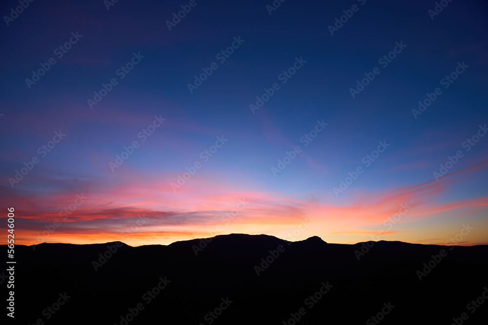 Landscape long exposure of majestic clouds in the sky sunset or sunrise over mountains. Beautiful colourful cloudscape scenery with silhouette of mountains. Amazing light of nature background