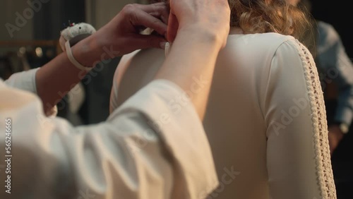 Close-up shot of tailor zipping up wedding dress on woman in front of mirror. Bride on fitting wedding dress in luxury designer atelier or wedding salon. Concept of fashion, handmade and couturier.