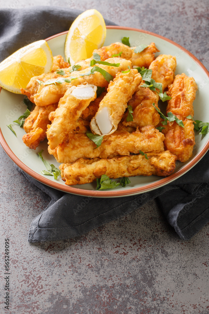 Battered and fried golden squid strips with lemon closeup on the plate on the table. Vertical Battered and fried golden squid strips with lemon closeup on the plate on the table. Vertical