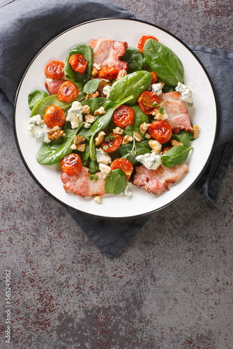 Salad with bacon, spinach, roquefort cheese, walnuts, tomatoes, basil and garlic close-up in a plate on the table. Vertical top view from above
