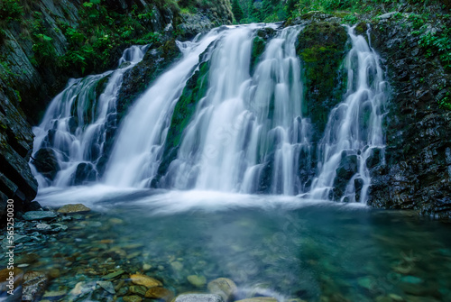 Beautiful mountain rainforest waterfall with fast flowing water and rocks  long exposure. Natural seasonal travel outdoor background with sun shining. Stream waterfall on rocks in the forest
