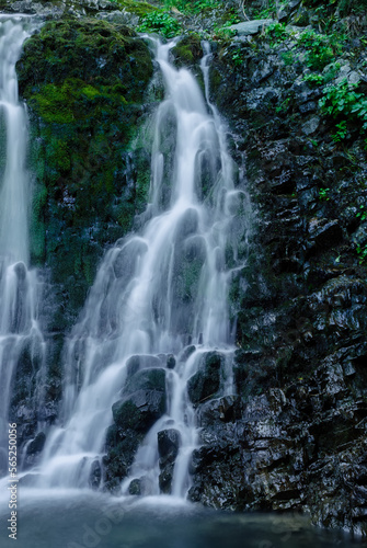 Beautiful mountain rainforest waterfall with fast flowing water and rocks  long exposure. Natural seasonal travel outdoor background with sun shining. Stream waterfall on rocks in the forest