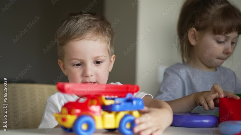 Happy family. Puzzle game. Colored toy in the hands of children. Teaching children in kindergarten. Boys and girls teamwork build cubes. Colored blocks and toy car on table in kindergarten. Schooling Happy family. Puzzle game. Colored toy in the hands of children. Teaching children in kindergarten. Boys and girls teamwork build cubes. Colored blocks and toy car on table in kindergarten. Schooling