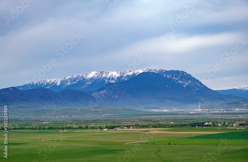 Beautiful aerial view of the snowcapped Piatra Craiului mountains (Brasov, Romania) from Rasnov in springtime. Idyllic alpine mountain scenery with large green valley, villages and high mountains