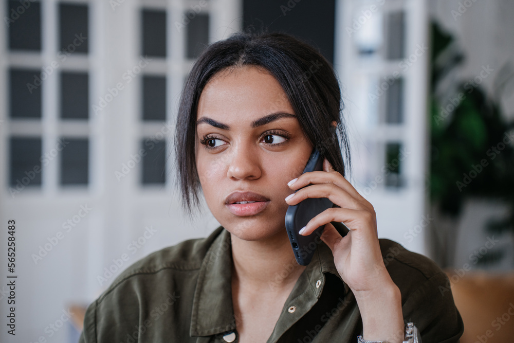 Close up of young African American Wiman talking by phone at home dressed in casual. Perplexed Brazilian girl tired, disapointed by bad news. Female entrepreneur discussing with partner. Close up of young African American Wiman talking by phone at home dressed in casual. Perplexed Brazilian girl tired, disapointed by bad news. Female entrepreneur discussing with partner.