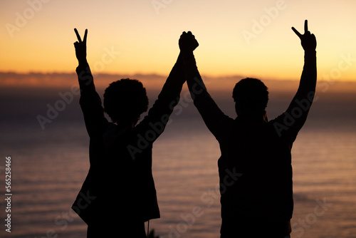 Sunset, beach and silhouette of couple celebration, success or winning and holding hands in shadow, night or dark. Sky, ocean and winner people in rear with peace sign for sea, hiking or travel goals
