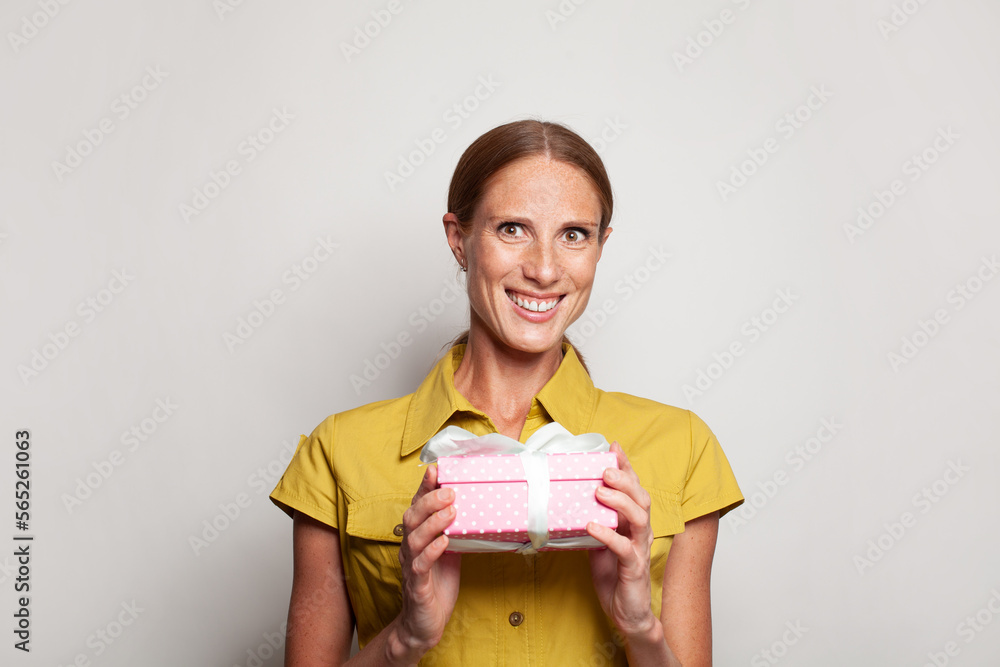 Attractive optimistic happy smiling woman with pink gift present box with white ribbon against white studio wall  banner background
