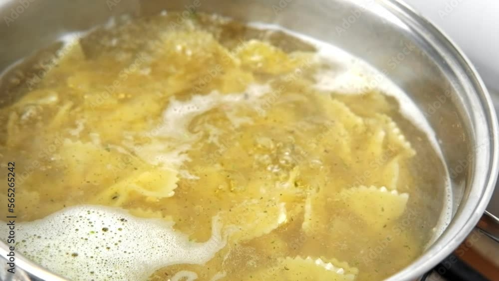 Boiling pasta in a saucepan. Whole wheat Farfalle, bow-tie or butterfly pasta Cooking in a pot with Steaming boiling water. Preparing Italian dish. Pan on a stove. High angle view. Slow Motion footage Boiling pasta in a saucepan. Whole wheat Farfalle, bow-tie or butterfly pasta Cooking in a pot with Steaming boiling water. Preparing Italian dish. Pan on a stove. High angle view. Slow Motion footage