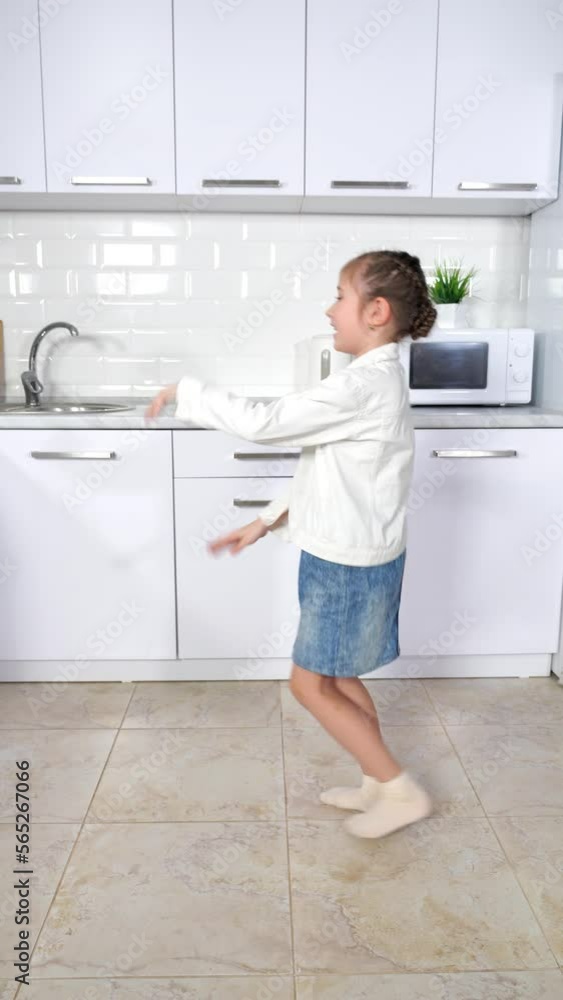 Junior schoolgirl enjoys dancing against shelves in kitchen. Happy daughter with amused and excited expressions demonstrates amazing moves Junior schoolgirl enjoys dancing against shelves in kitchen. Happy daughter with amused and excited expressions demonstrates amazing moves