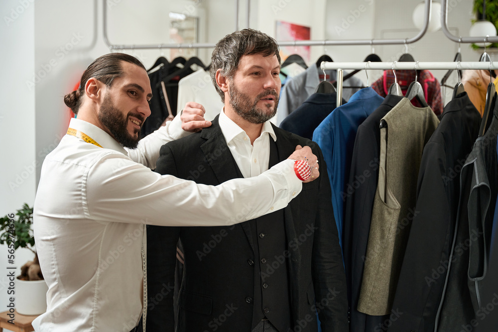 Pleased tailor trying on new suit on client Pleased tailor trying on new suit on client