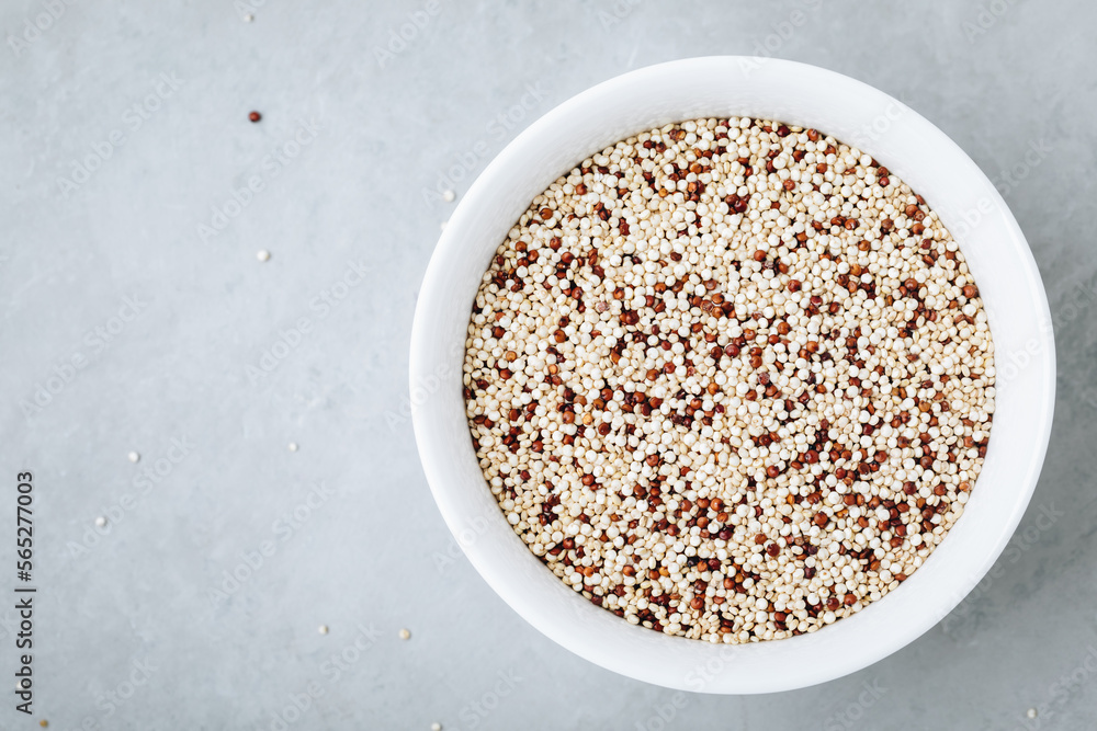 Quinoa. Red white brown quinoa seeds in bowl. Mixed organic raw quinoa seeds on gray stone background.