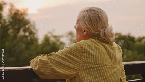 Pensive senior woman standing near fence alone, looking at sunset, life memories © Synthex🇺🇦