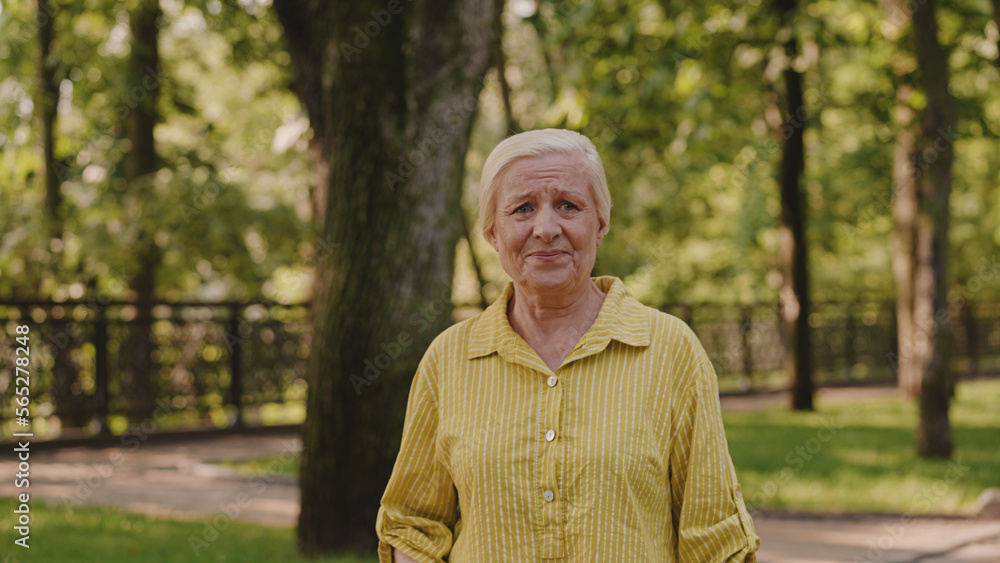 Aged woman standing alone in park, happy with recovery, breathing fresh air Aged woman standing alone in park, happy with recovery, breathing fresh air