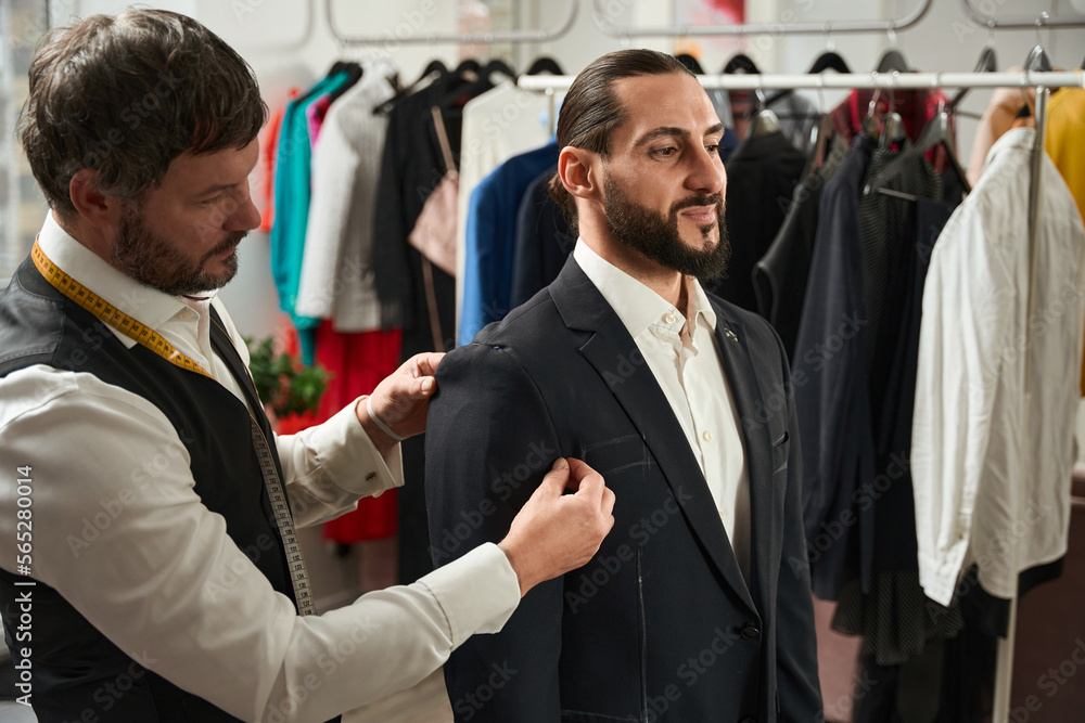 Experienced tailor trying on custom-made garment on man
