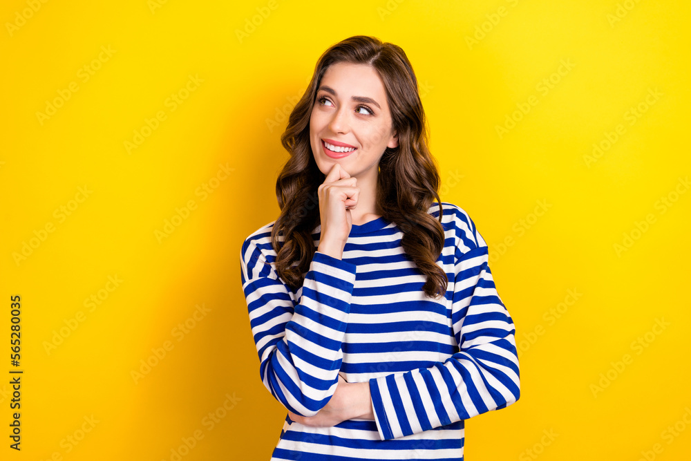 Photo portrait of attractive young woman touch chin look curious empty space wear trendy striped outfit isolated on yellow color background Photo portrait of attractive young woman touch chin look curious empty space wear trendy striped outfit isolated on yellow color background