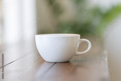 Hot latte coffee in white cup on wooden table, blurred background in cafe