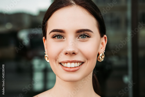 Pretty brunette caucasian woman standing outside street with white teeth beaming healthy smiling lady. Happy millennial girl model posing looking at the camera, head shot portrait. 