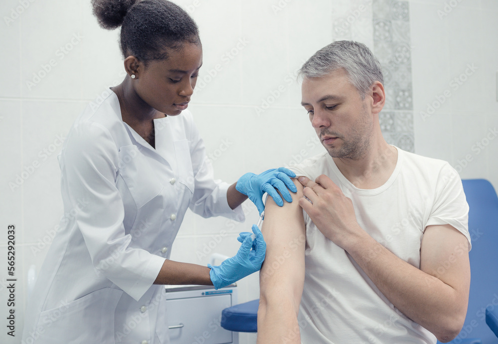 African-American female doctor gives an injection inoculation in the arm of a male patient. African-American female doctor gives an injection inoculation in the arm of a male patient.