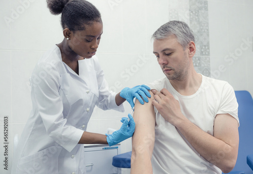 African-American female doctor gives an injection inoculation in the arm of a male patient.