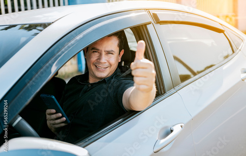 Smiling driver holding cellphone showing thumb up. Driver man showing thumb up while holding cellphone. Happy driver giving a thumbs up on the road. safe driving concept © IHERPHOTO