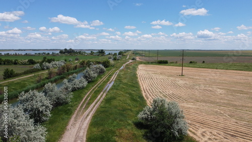 Dirt road near the river and endless fields. Summer. Beautiful Ukrainian nature. High quality aerial photo