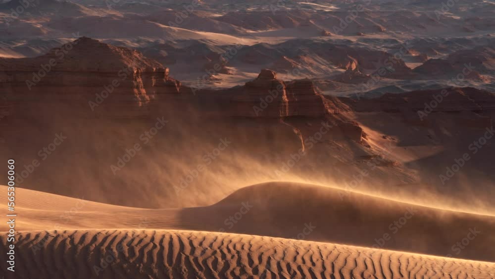 Sand blowing over dunes in wind, red cliffs on background, Gobi desert. Mongolia