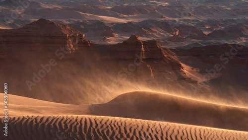 Sand blowing over dunes in wind, red cliffs on background, Gobi desert. Mongolia