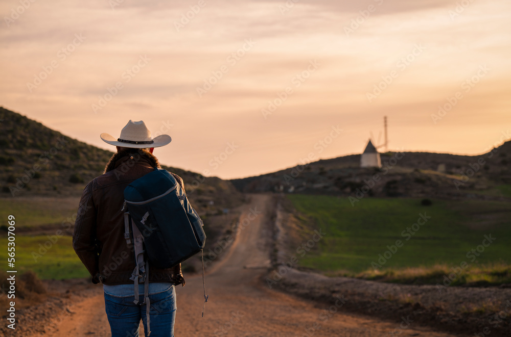 Adult man in cowboy hat walking on dirt road against sky during sunrise
