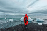 A female tourist in a red jacket walks near glaciers in the Jokulsarlon glacial lagoon near Vatnajokull National Park, southeast Iceland .Trip Iceland