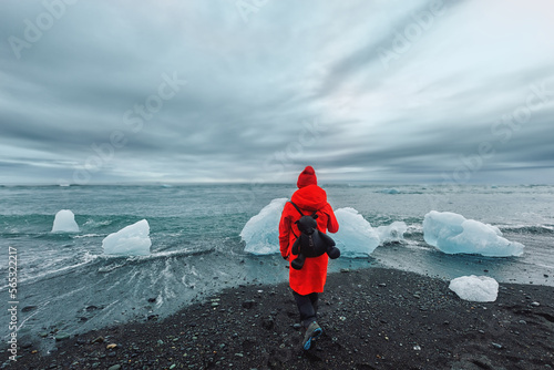 A female tourist in a red jacket walks near glaciers in the Jokulsarlon glacial lagoon near Vatnajokull National Park, southeast Iceland .Trip Iceland photo