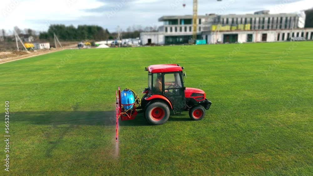 The tractor sprinkles the grass of the football field. Maintenance of the new soccer field and grass care. The tractor sprinkles the grass of the football field. Maintenance of the new soccer field and grass care.