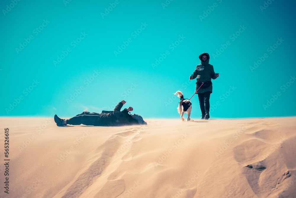 Happy boy and woman with dog playing on the sand dunes, turquise sky, copy space